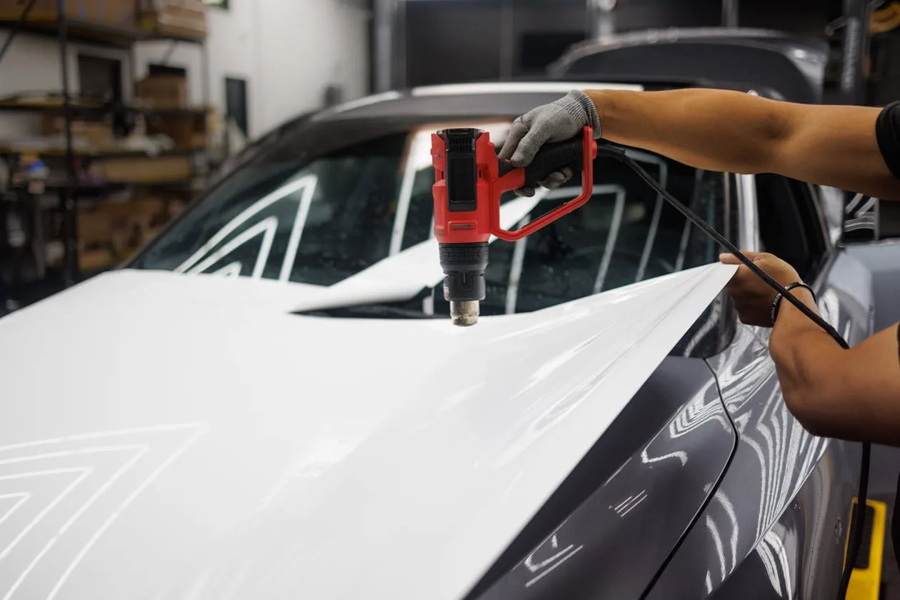 Technician applying vinyl wrap to a vehicle panel with a heat gun