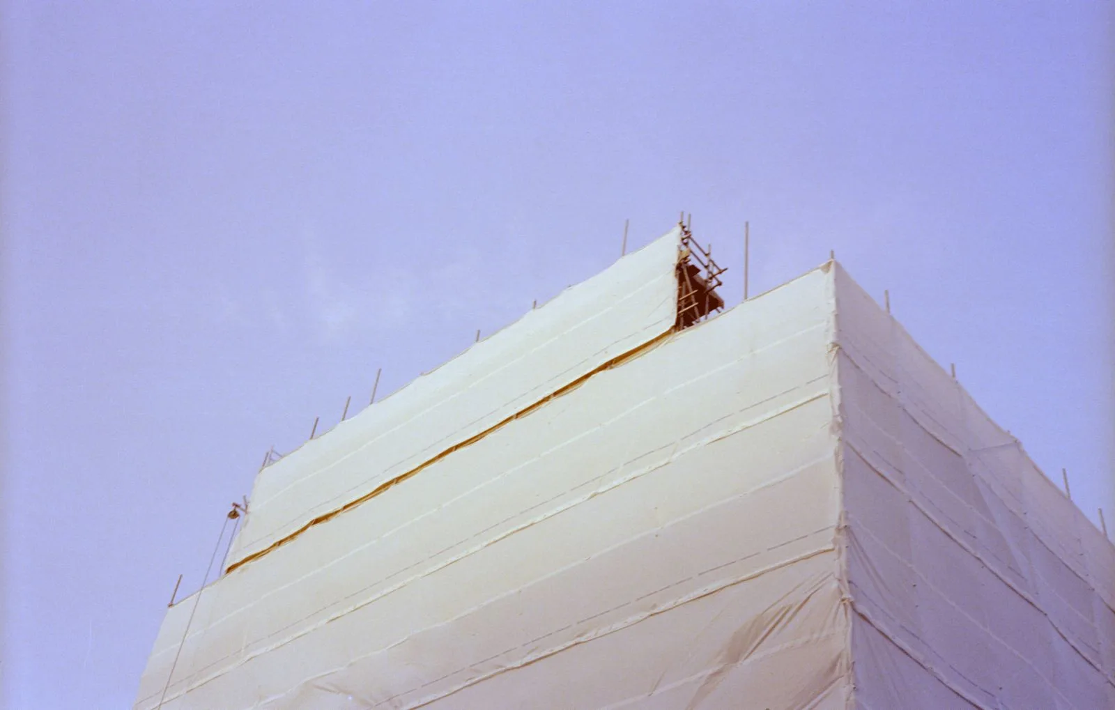 Building under construction wrapped in protective sheeting, low angle view against blue sky