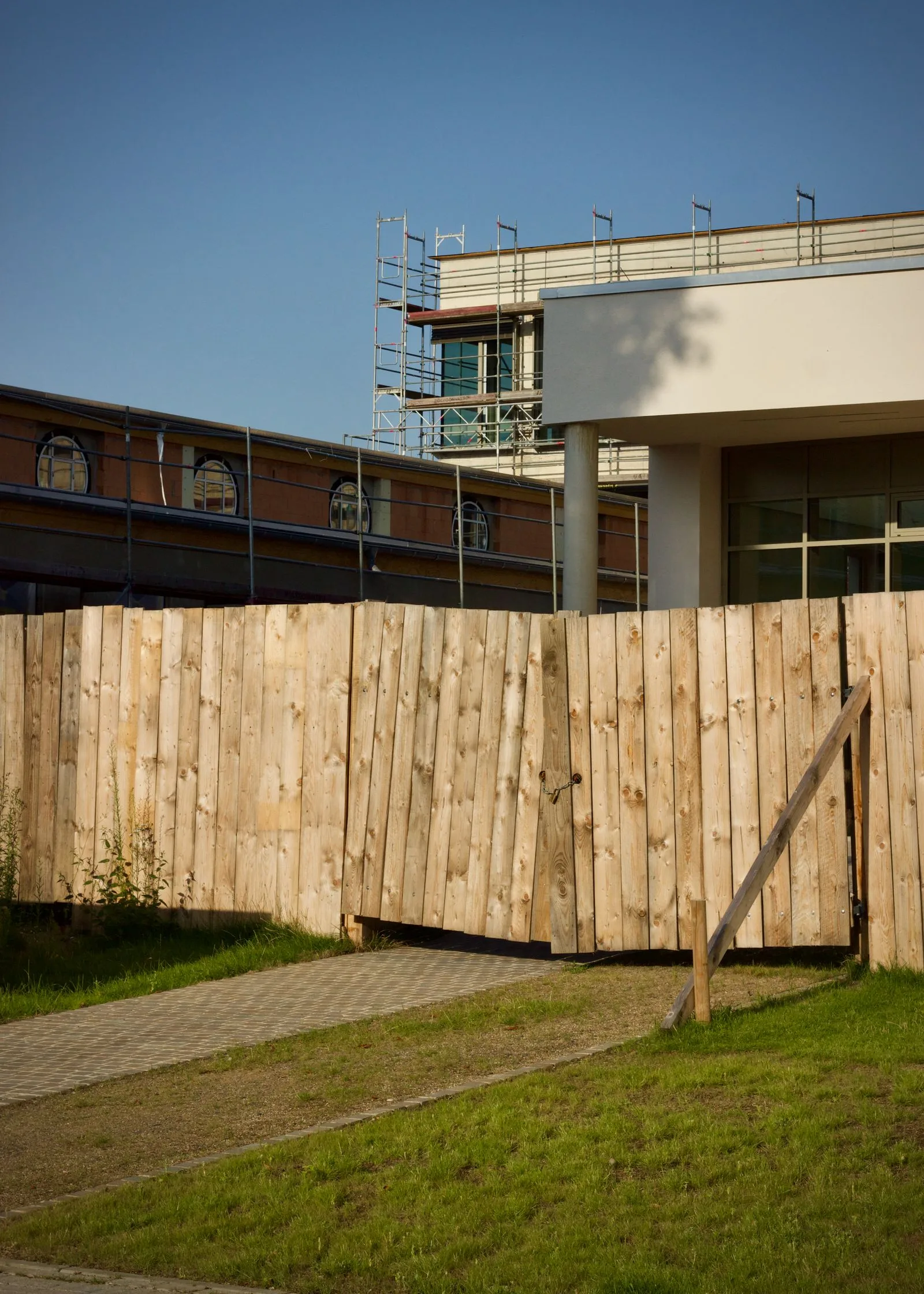 Construction site boundary hoarding with wooden fence and scaffolding visible from the street