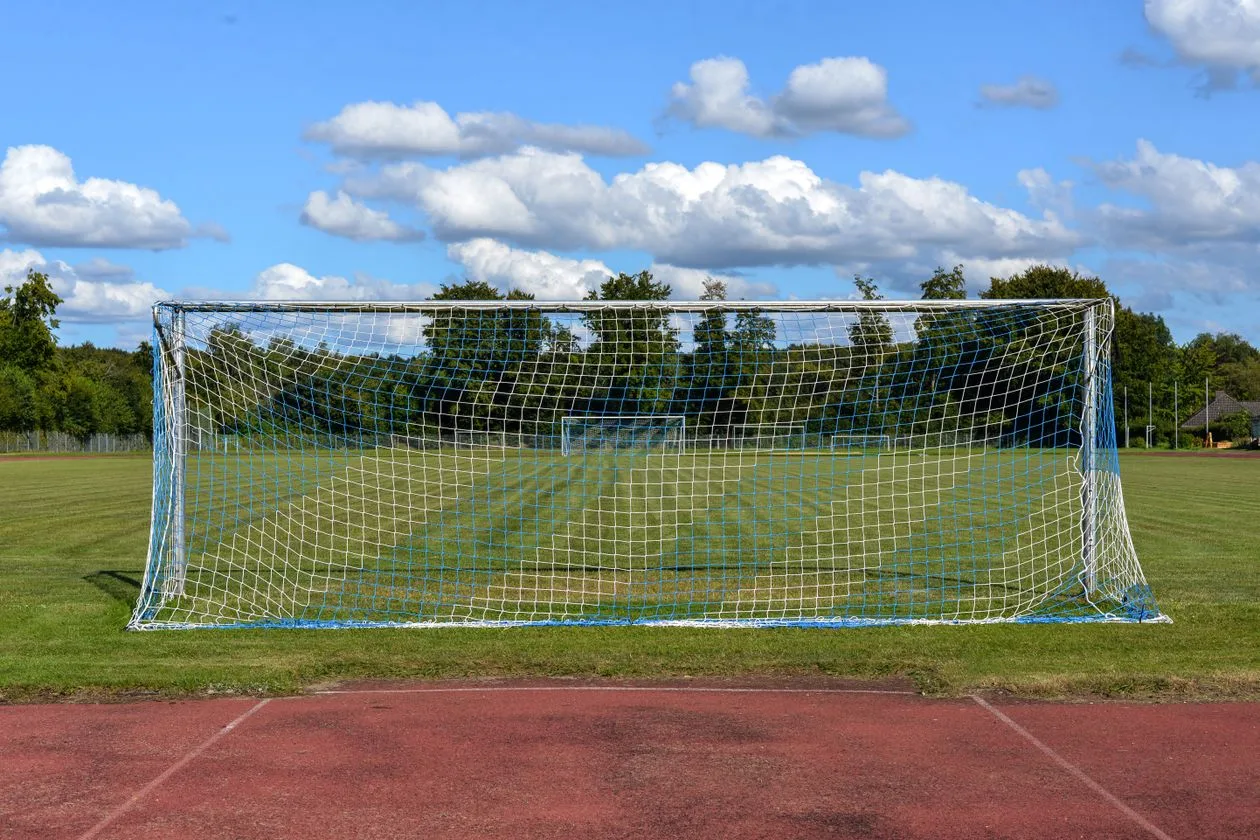 Empty football goal net on a grass pitch under a blue sky