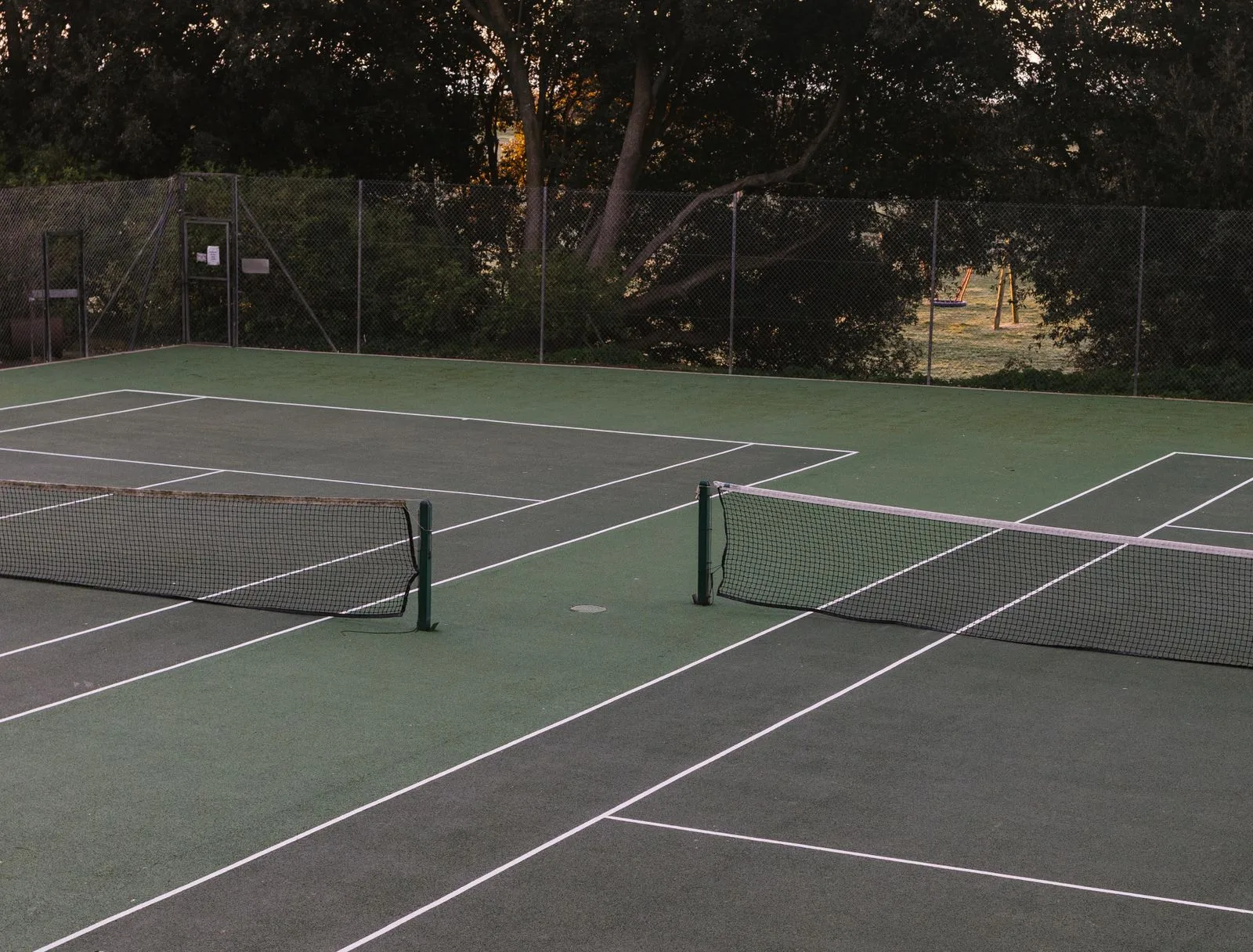 Empty outdoor tennis court surrounded by trees
