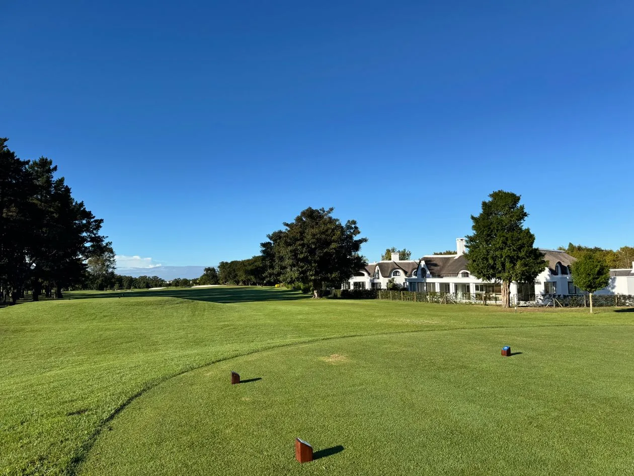 Golf course fairway with clubhouse, tee markers and mature trees under a clear sky
