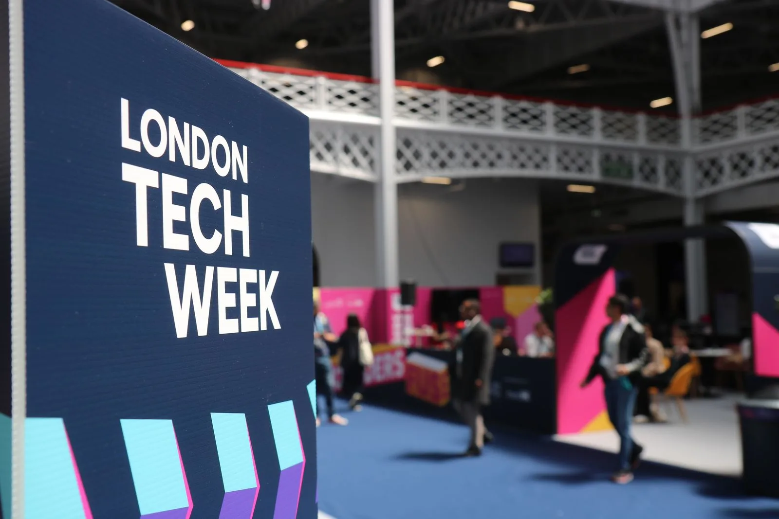 Bold event signage with a colourful exhibition stand backdrop blurred behind