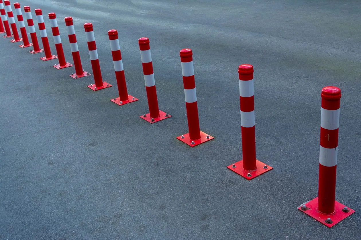 Row of red and white striped bollards on car park asphalt