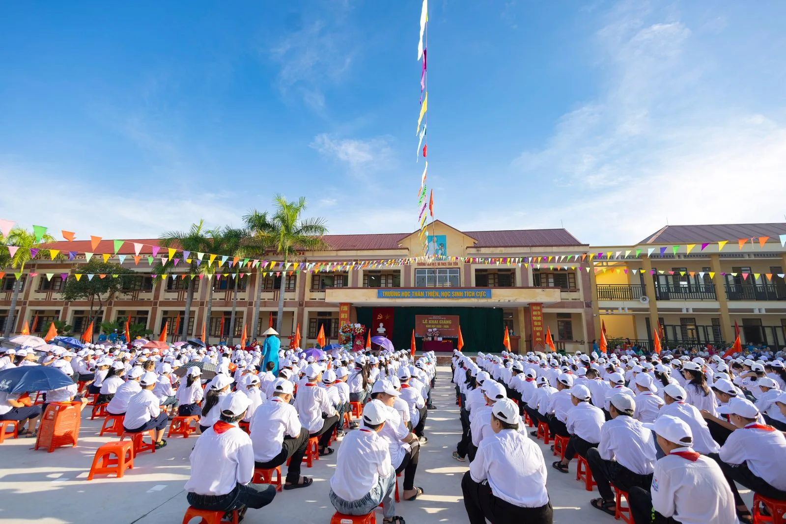 School assembly seated outdoors in a courtyard under a blue sky