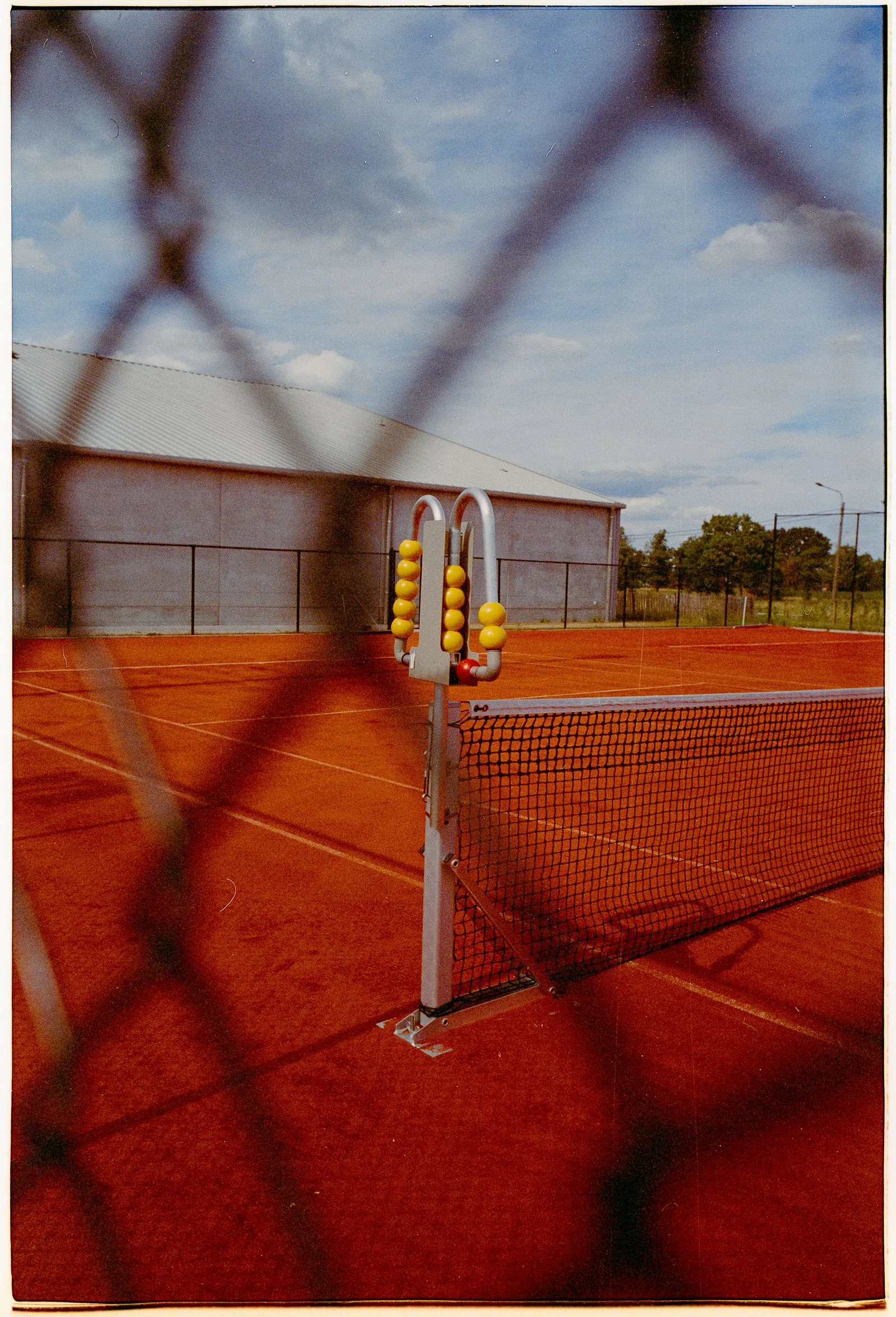 Tennis court net and clay surface seen through boundary fence
