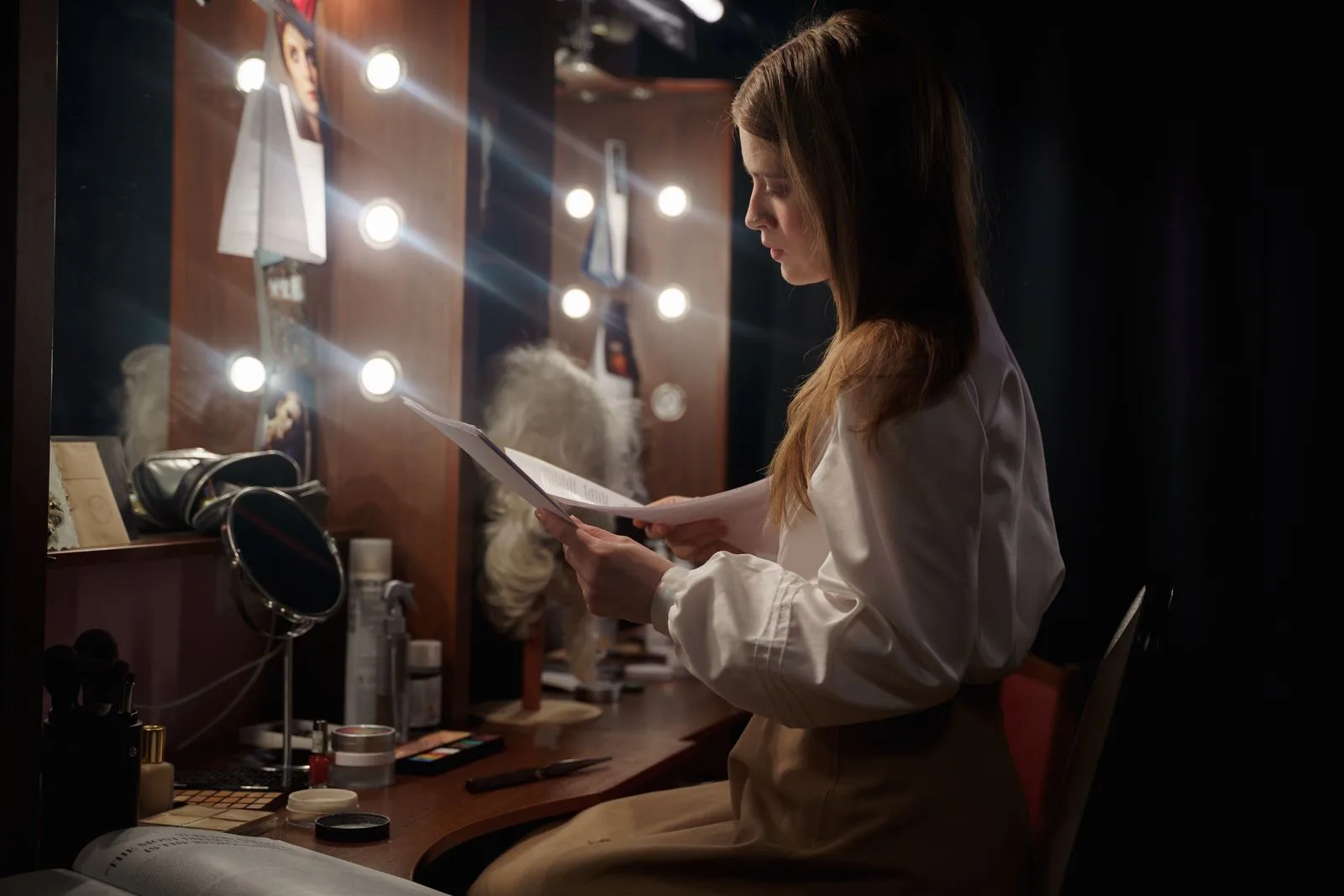 Performer reading a script in a theatre dressing room with mirror lights