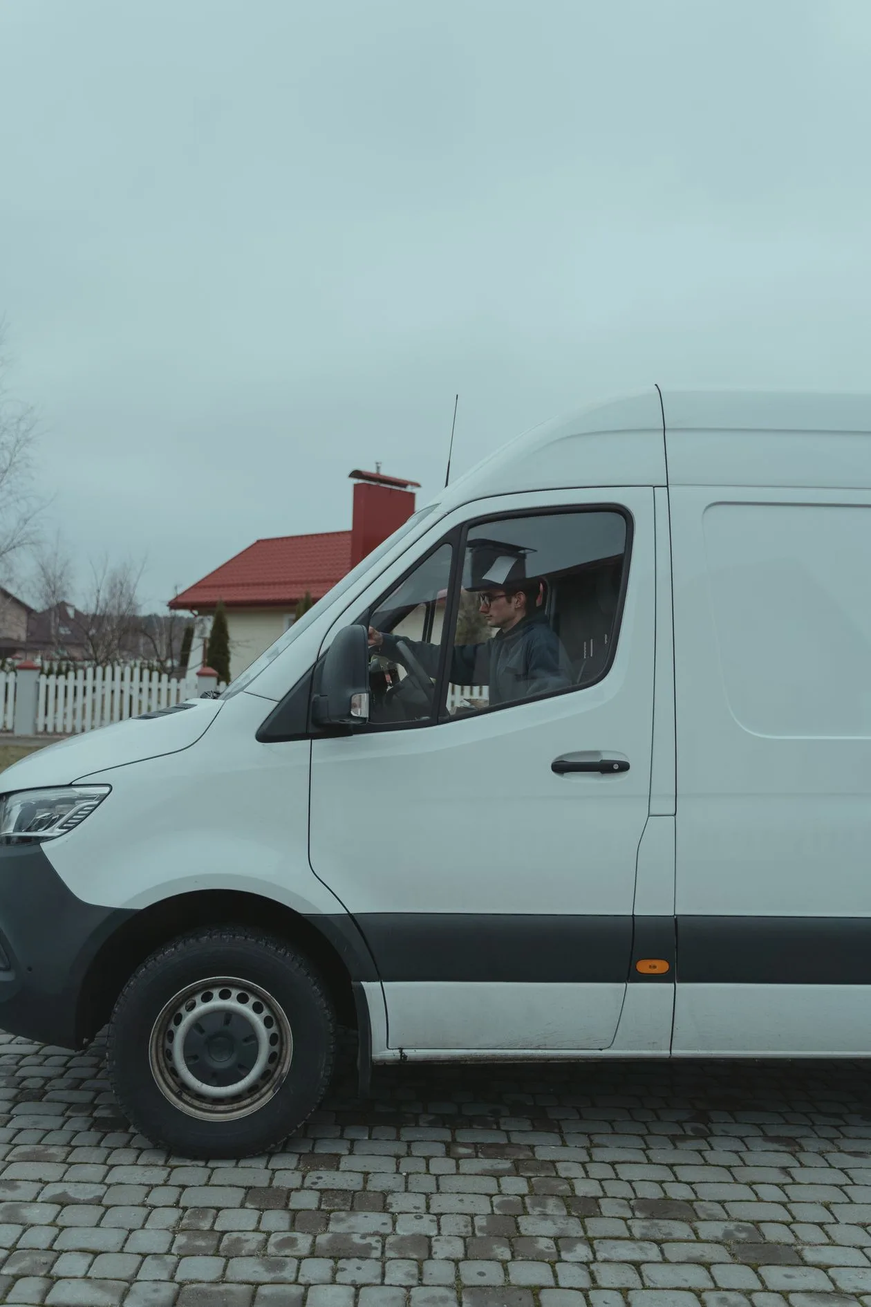 Tradesperson driving a plain white van on a cobbled street