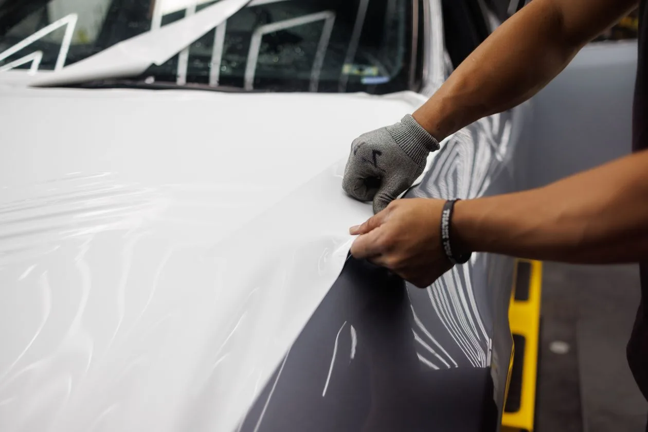 Hand using a squeegee to smooth vinyl wrap onto a car bonnet