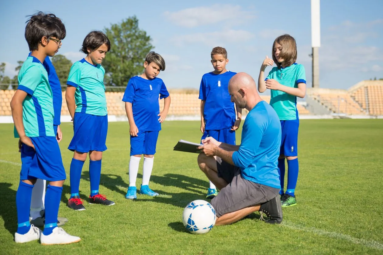 Coach guiding young football players in matching training kit on a green field