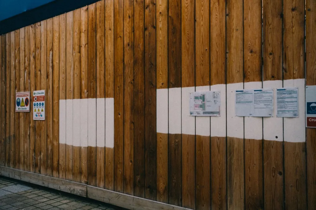 Wooden construction hoarding fence with printed notices and safety signs attached